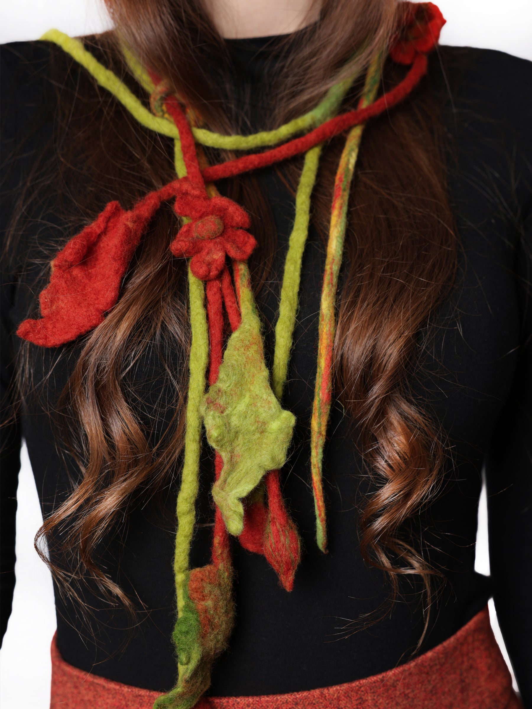 Close-up of a handmade wool neckpiece with green tones and red accents, showing sculptural floral texture.