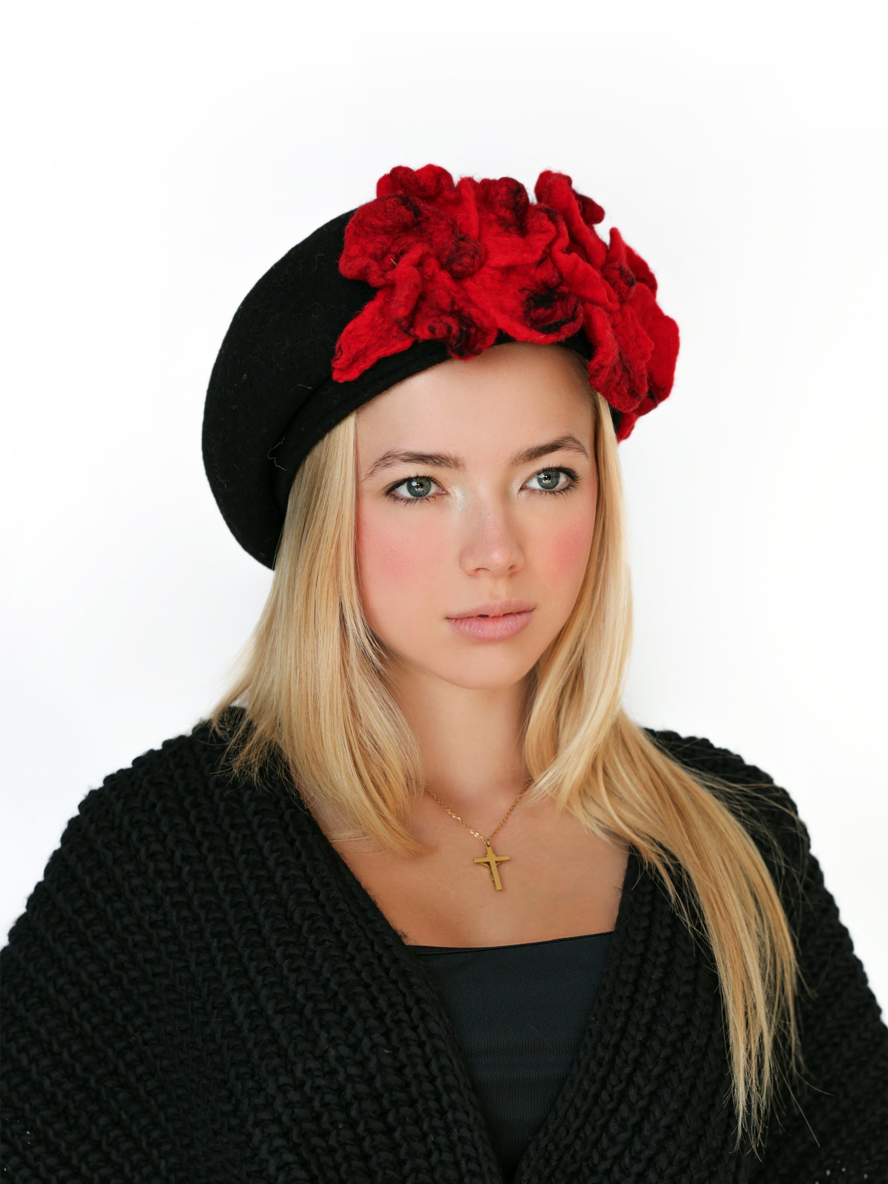 Angled view of a black wool beret hat featuring sculptural red felt flowers.