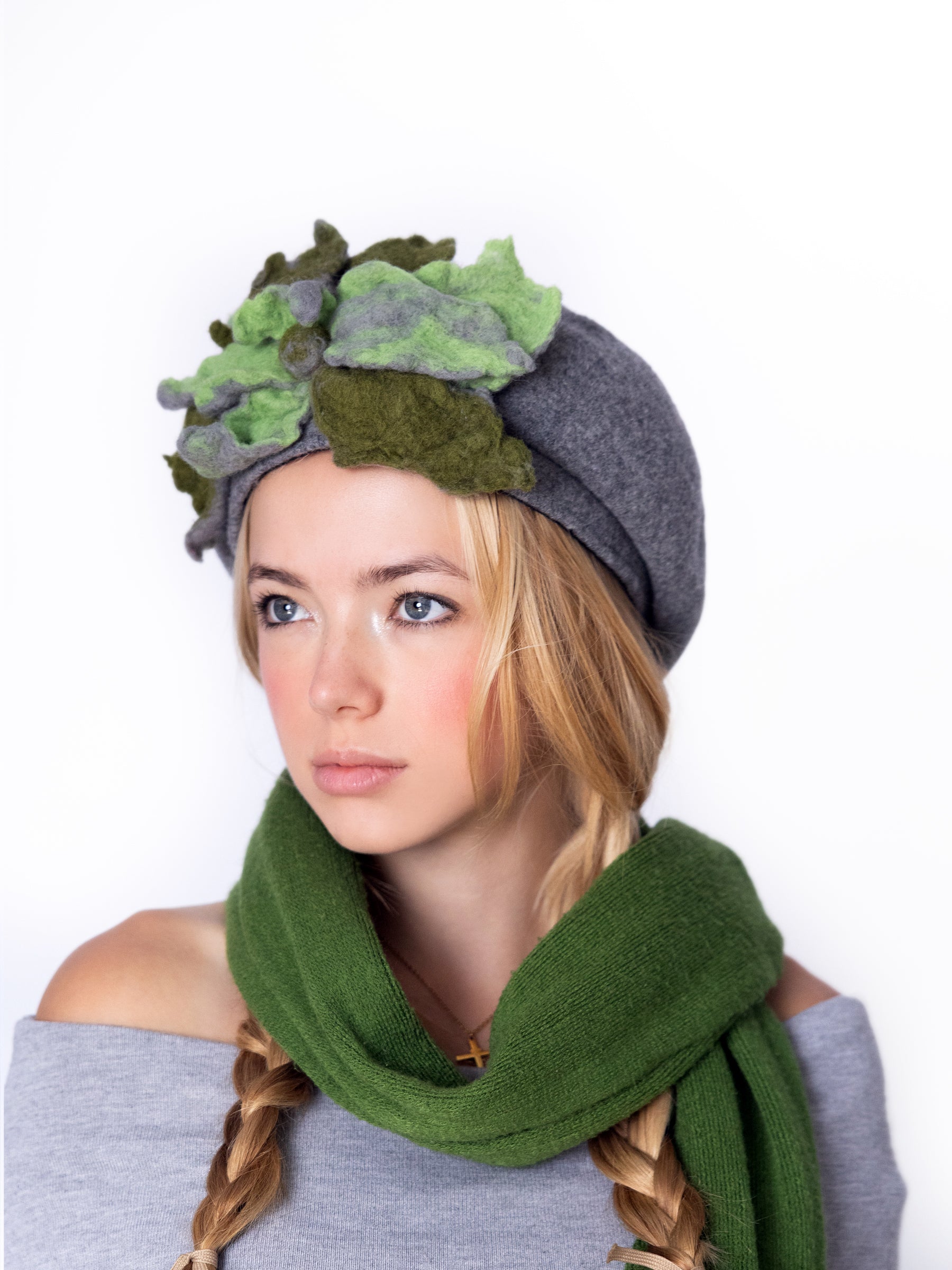Angled view of a grey wool beret hat with layered green and olive felt floral embellishment.