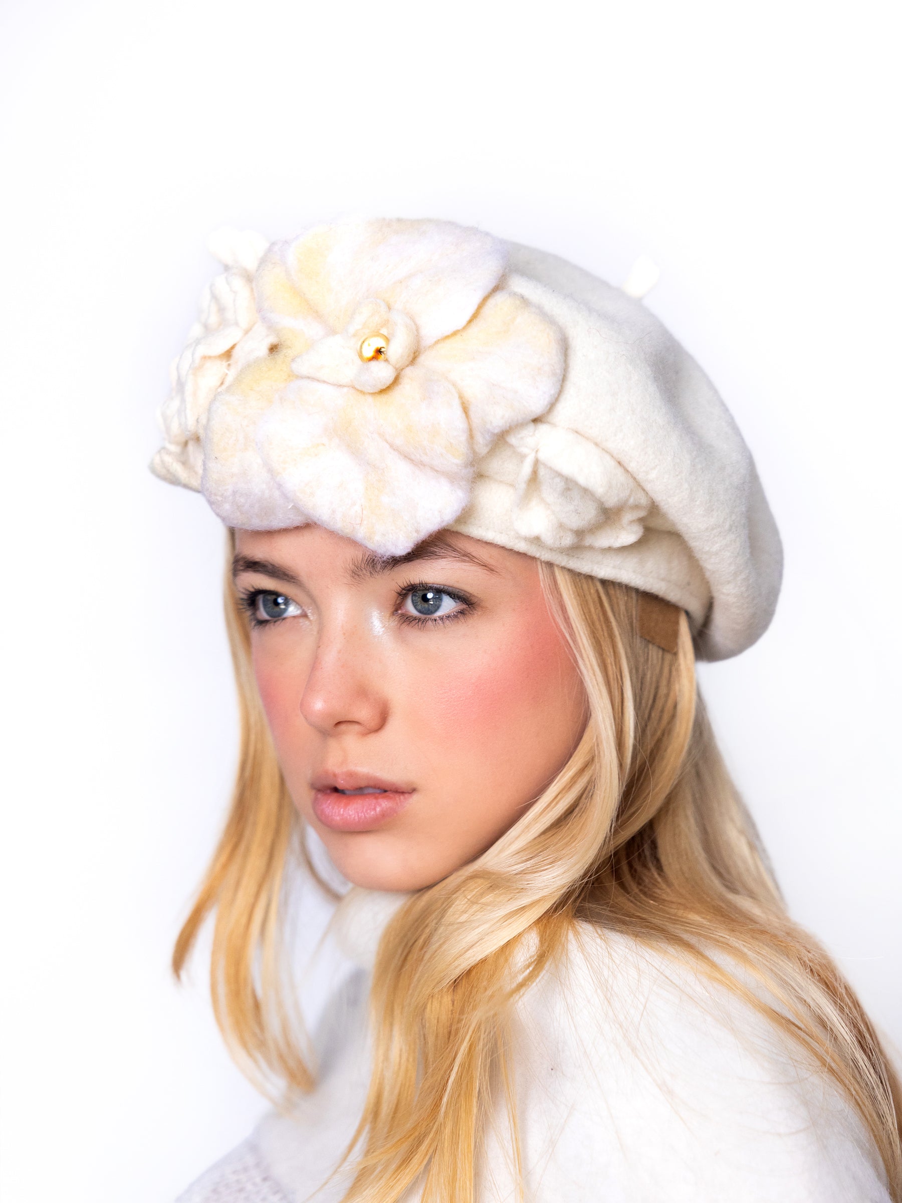 Side view of a white wool beret hat with layered ivory felt floral embellishment.