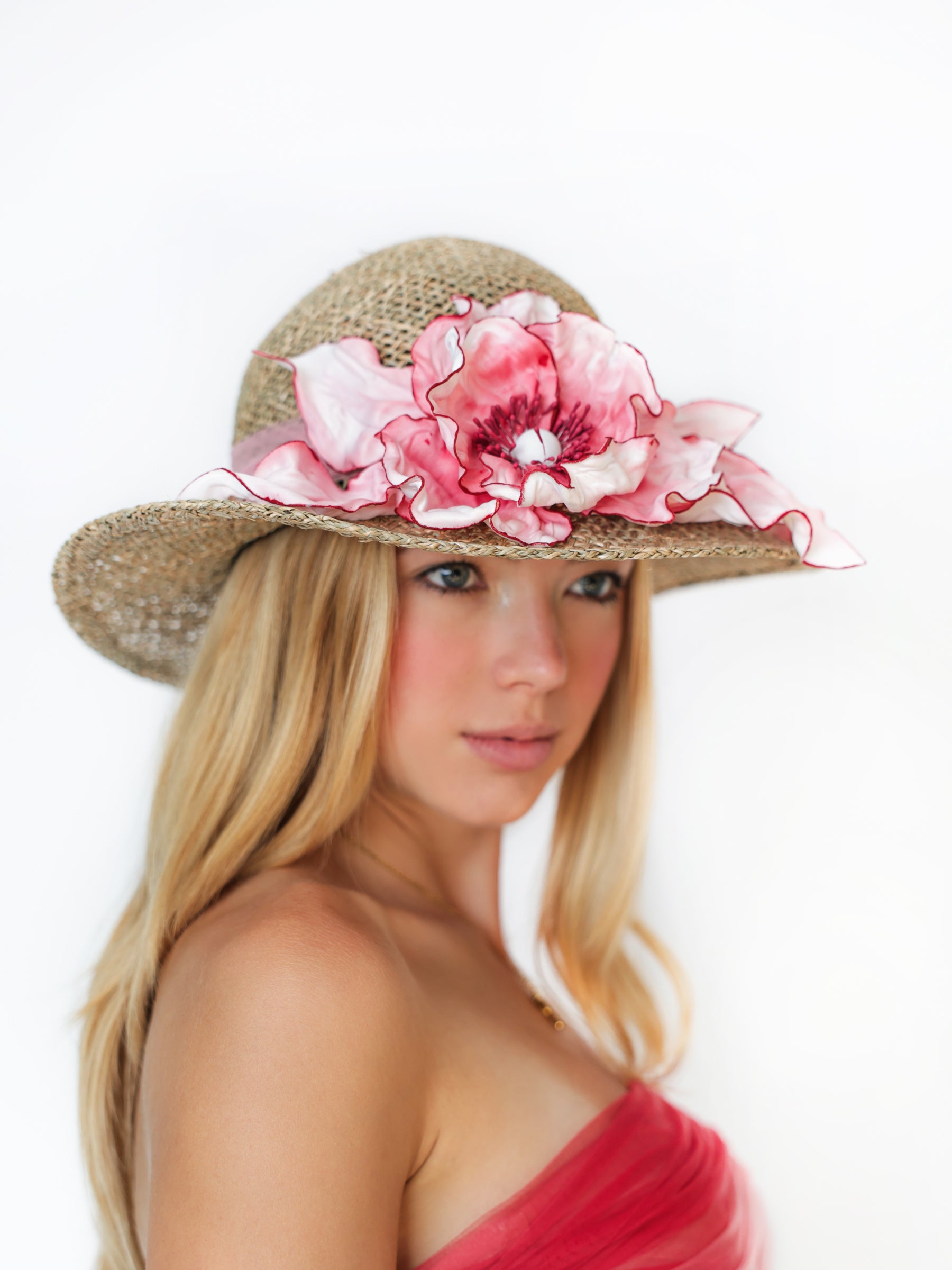 Side view of a straw summer hat with soft pink satin floral embellishment.