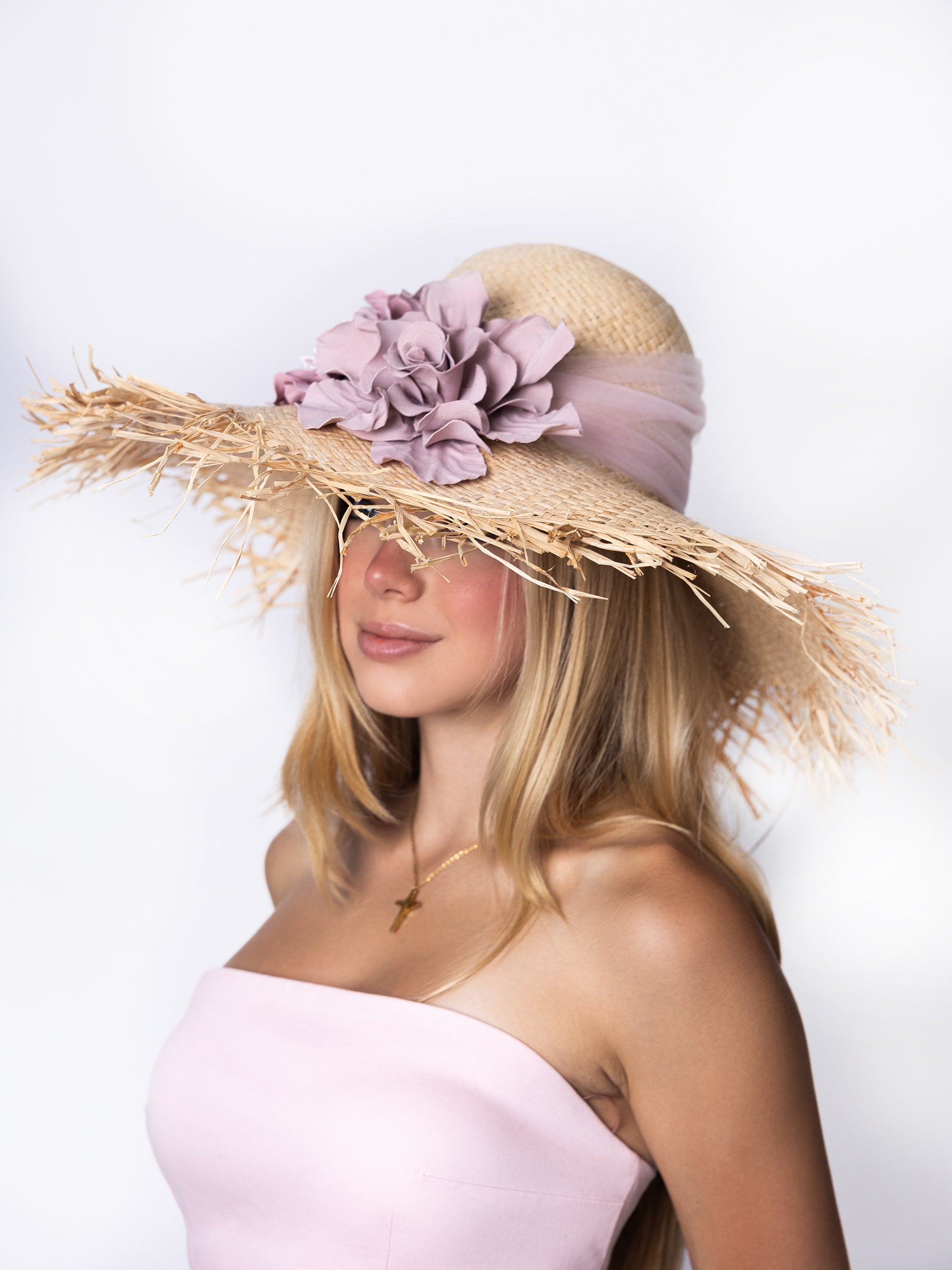 Side view of a straw wide-brim summer hat with hand-painted satin floral embellishment.