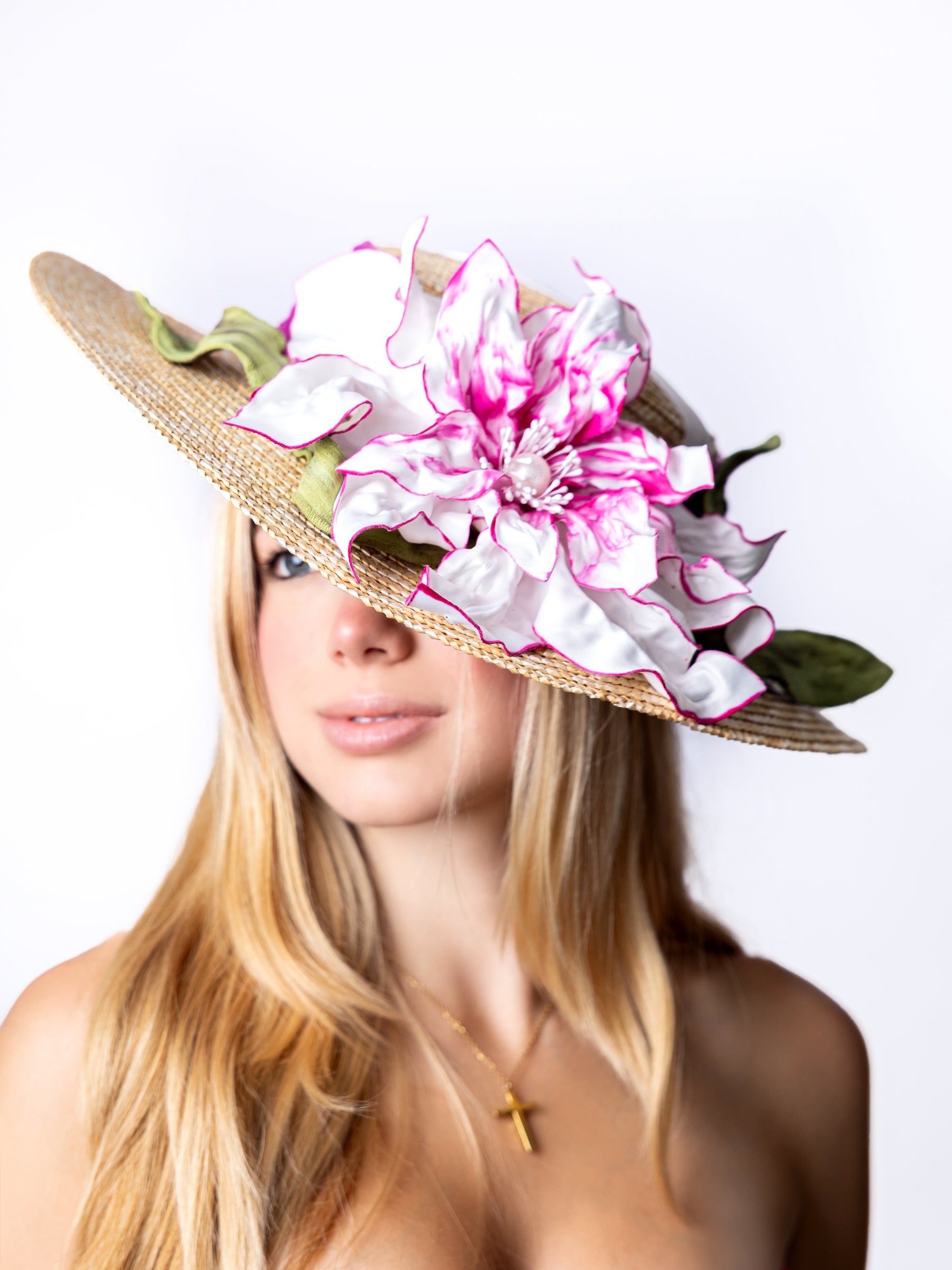Side view of a straw summer sun hat with pink and white satin floral accents.