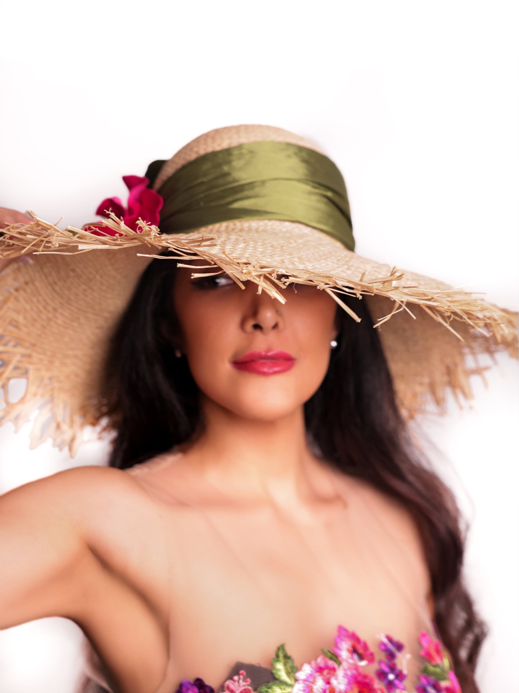 Front view of a straw summer hat highlighting the handmade red satin flower and wide brim.