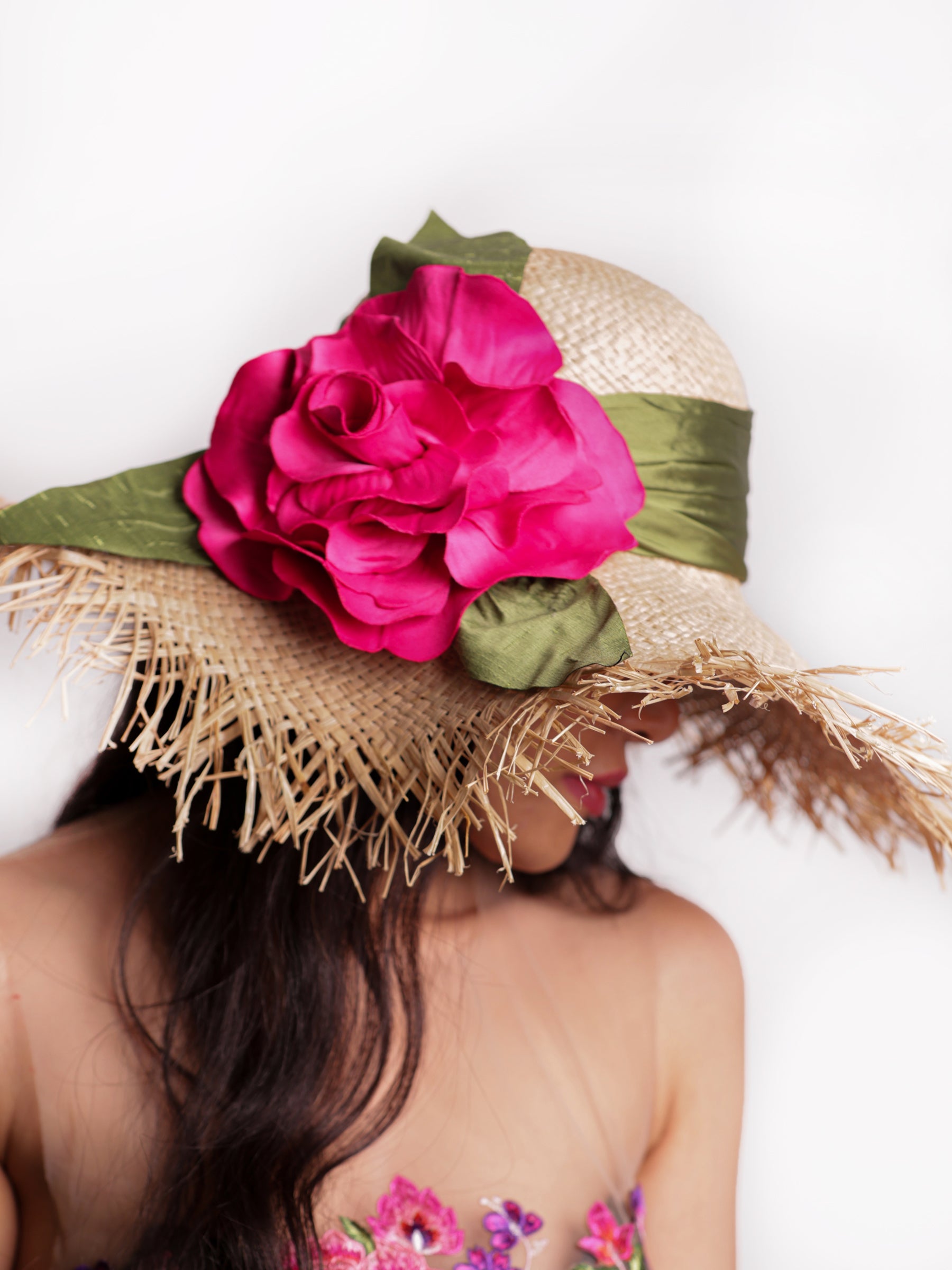 Angled view of a straw summer sun hat with bold red satin floral embellishment.