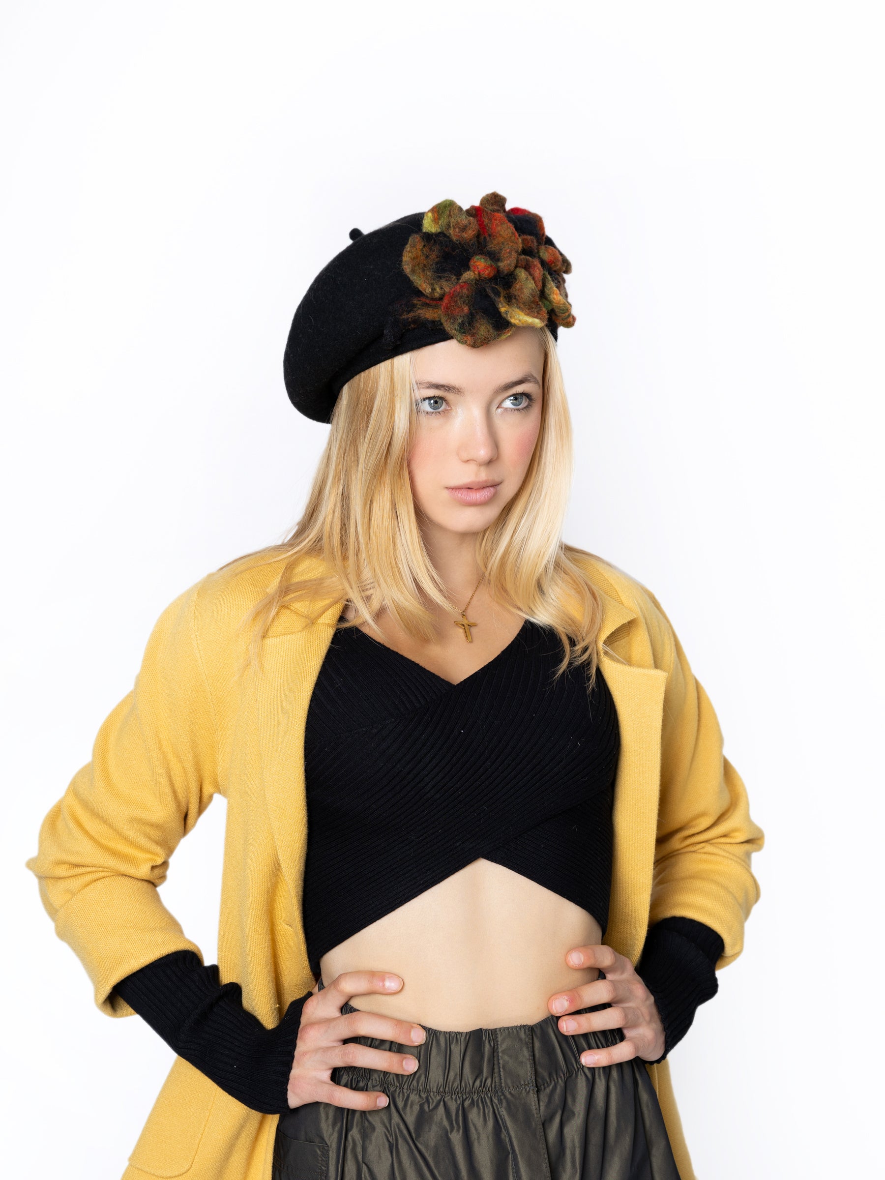 Model wearing a black wool beret hat with multicolor handmade felt floral detail, angled view.