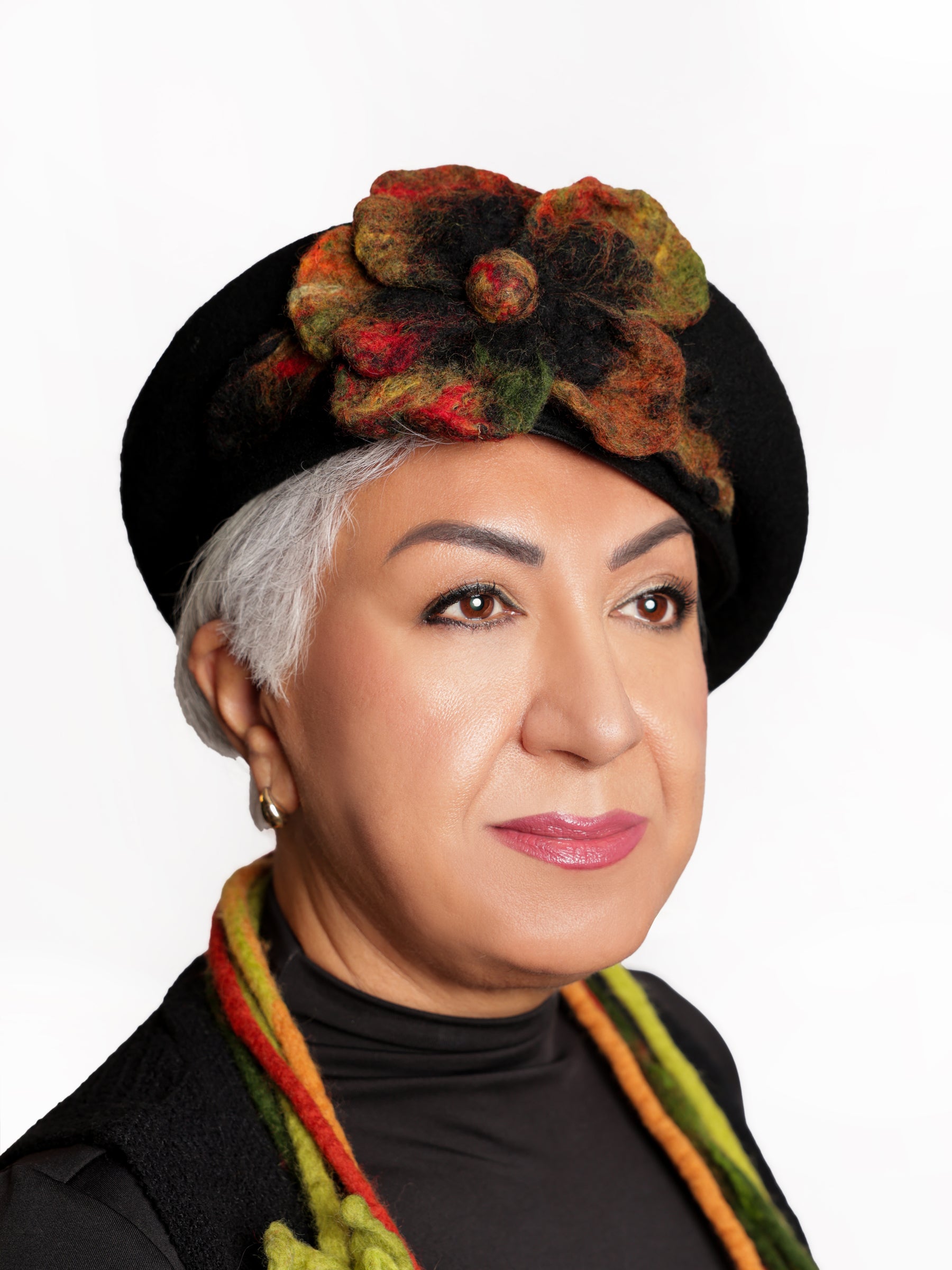 Side view of a woman wearing a handmade black wool beret with a sculptural multicolour felt flower.