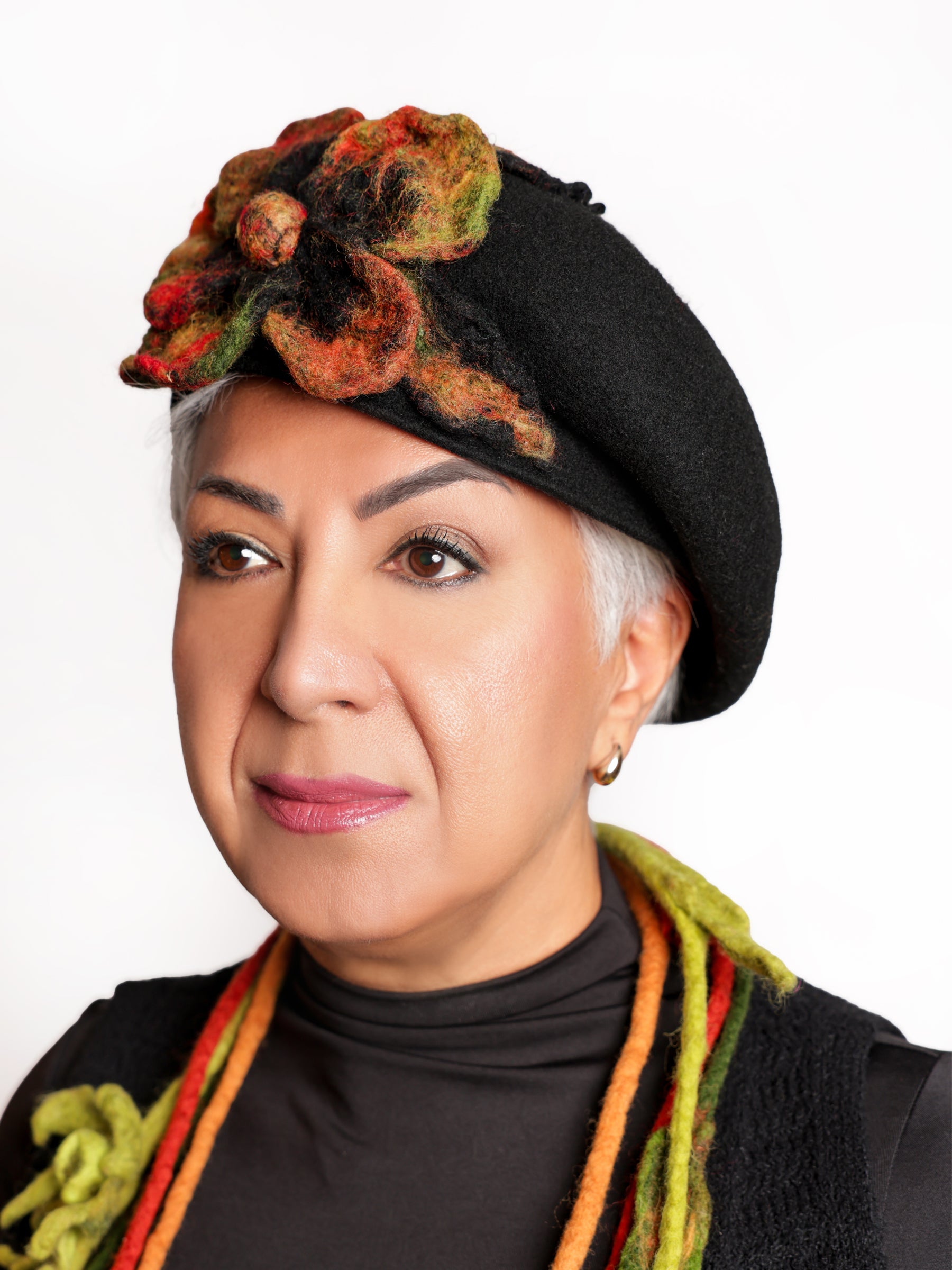 Left side view of a woman wearing a black wool beret with a textured multicolour felt flower.