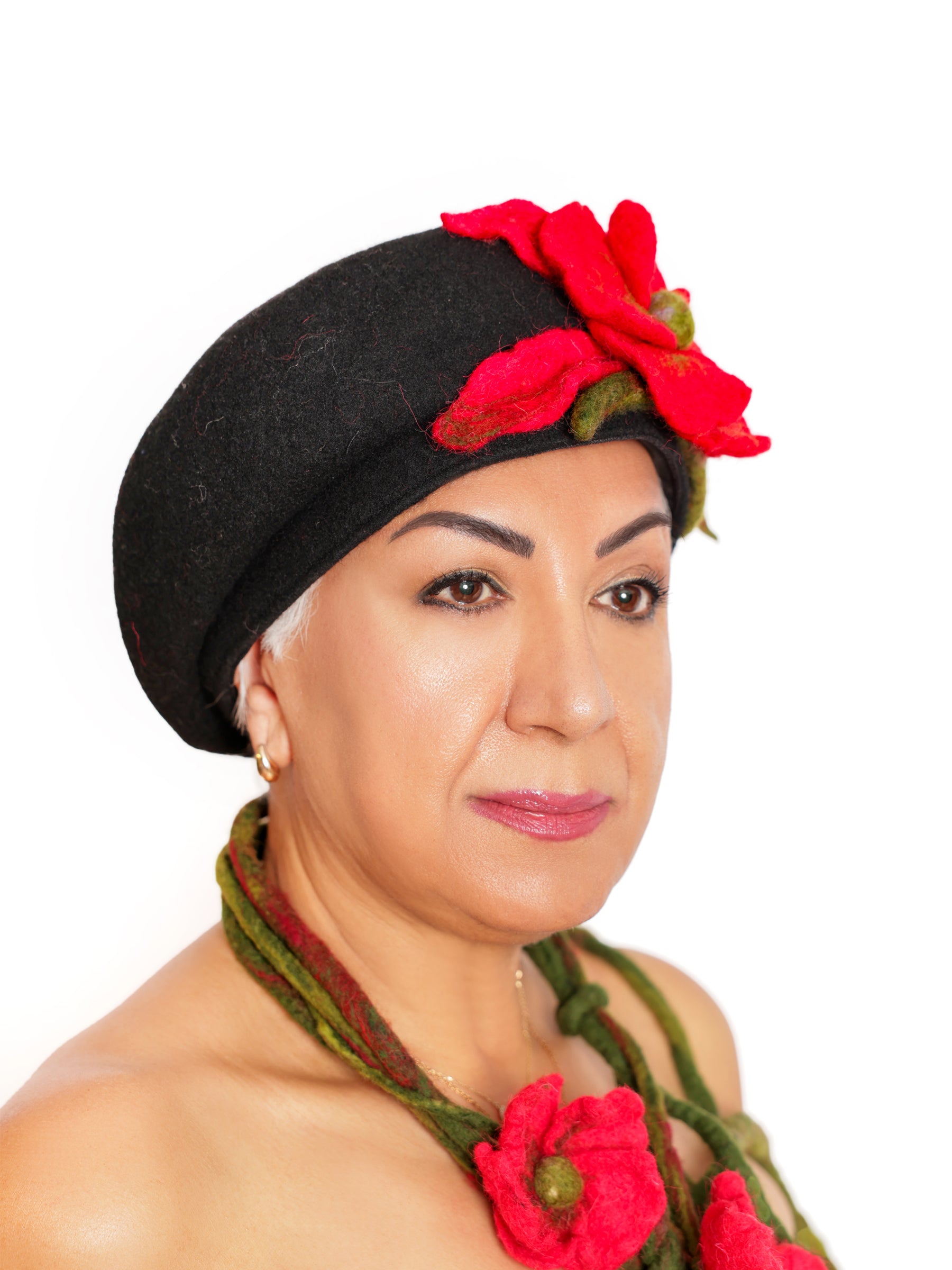 Angled side view of a black wool beret featuring a handmade red felt flower with soft olive-green detailing.