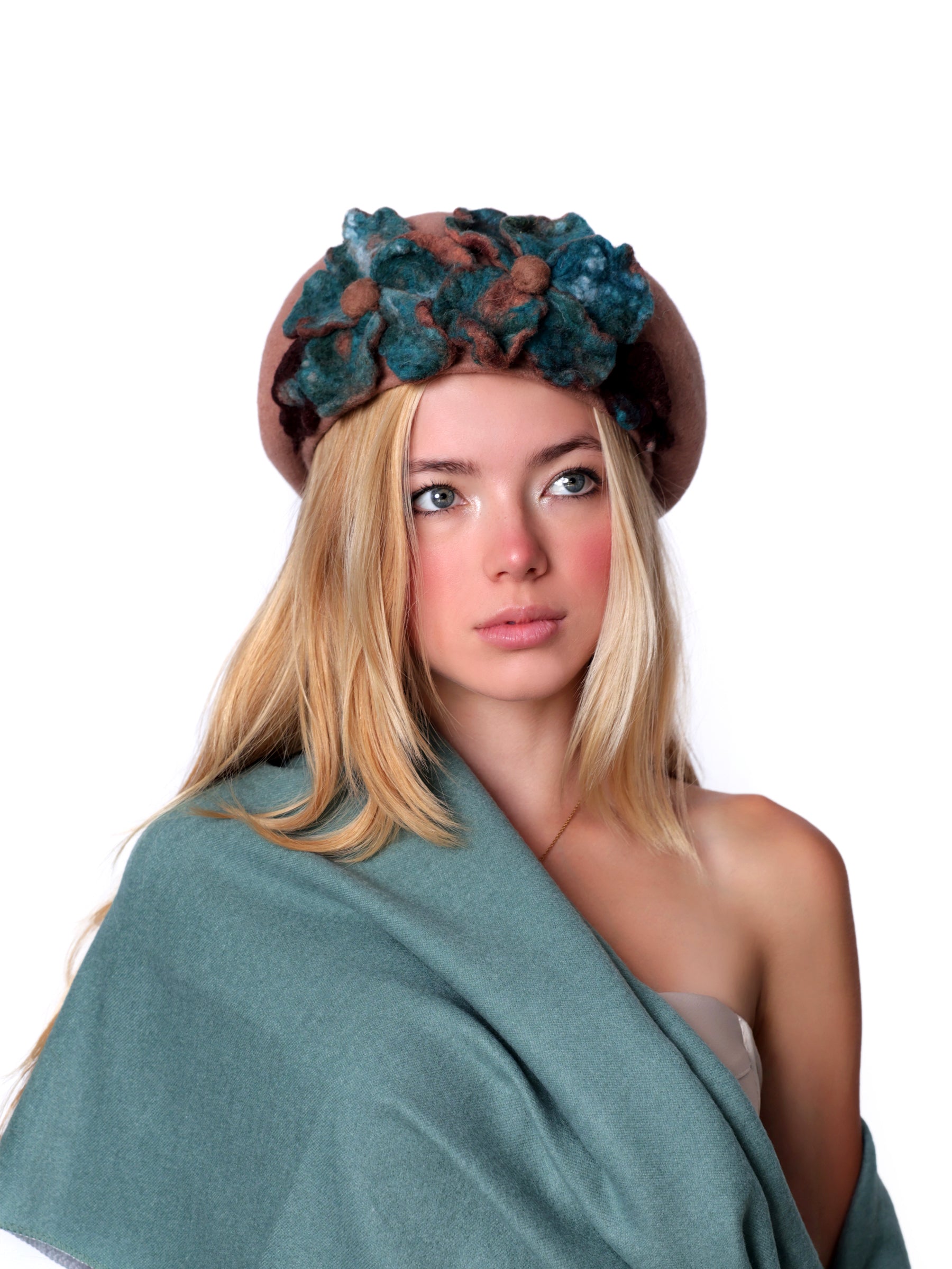 Model wearing a camel-toned wool beret hat with handmade teal and chestnut felt floral detail, front view.