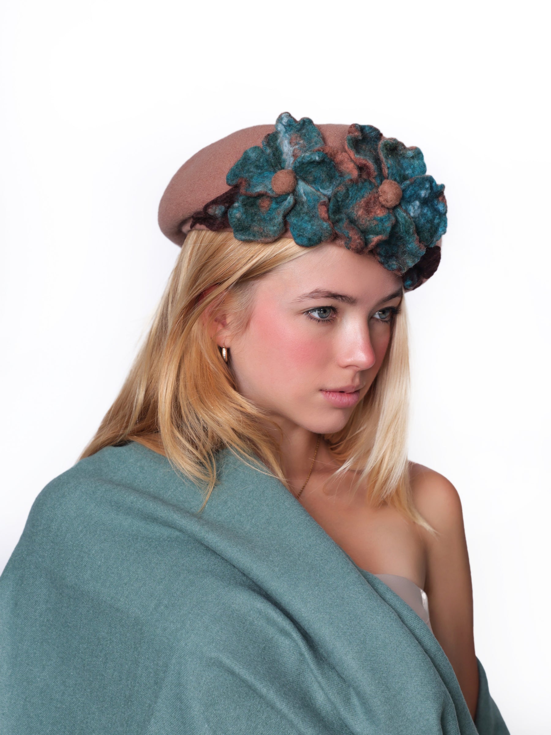Angled view of a wool beret hat in light brown tones with sculptural handmade felt flowers.