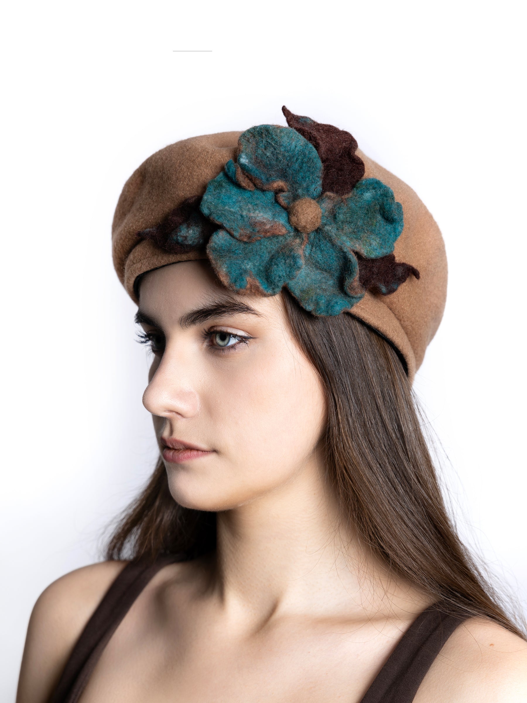Model wearing a beige wool beret hat with handmade felt floral detail in teal and brown tones.