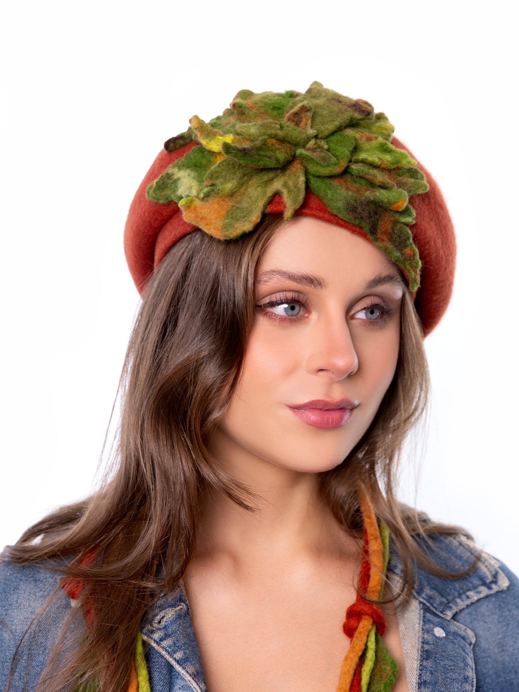 Model wearing a burnt orange wool winter beret hat with handmade green felt floral detail, angled view.