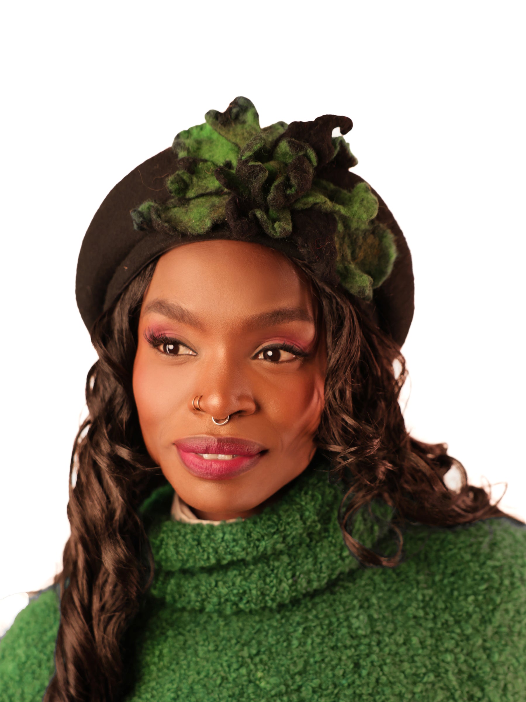 Handcrafted black winter beret with green floral accent, model looking slightly right, refined statement accessory.