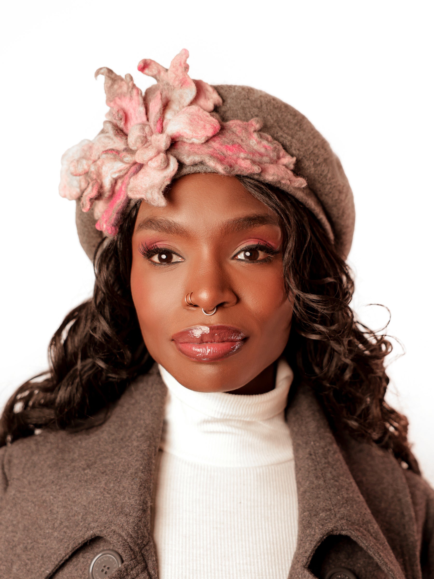 Model wearing a grey wool winter beret hat with handmade ash pink felt floral detail, front view.