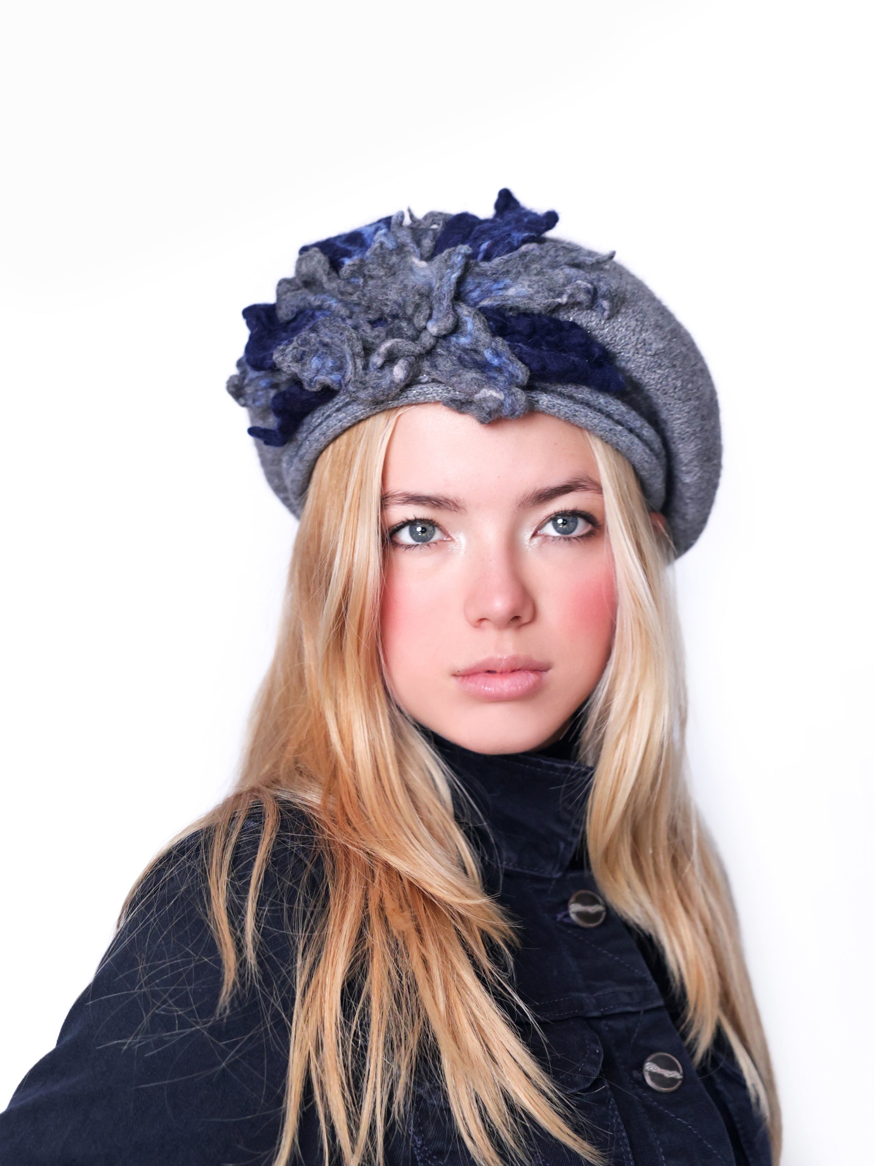 Model wearing a grey wool beret hat with handmade navy blue felt floral detail, front view.