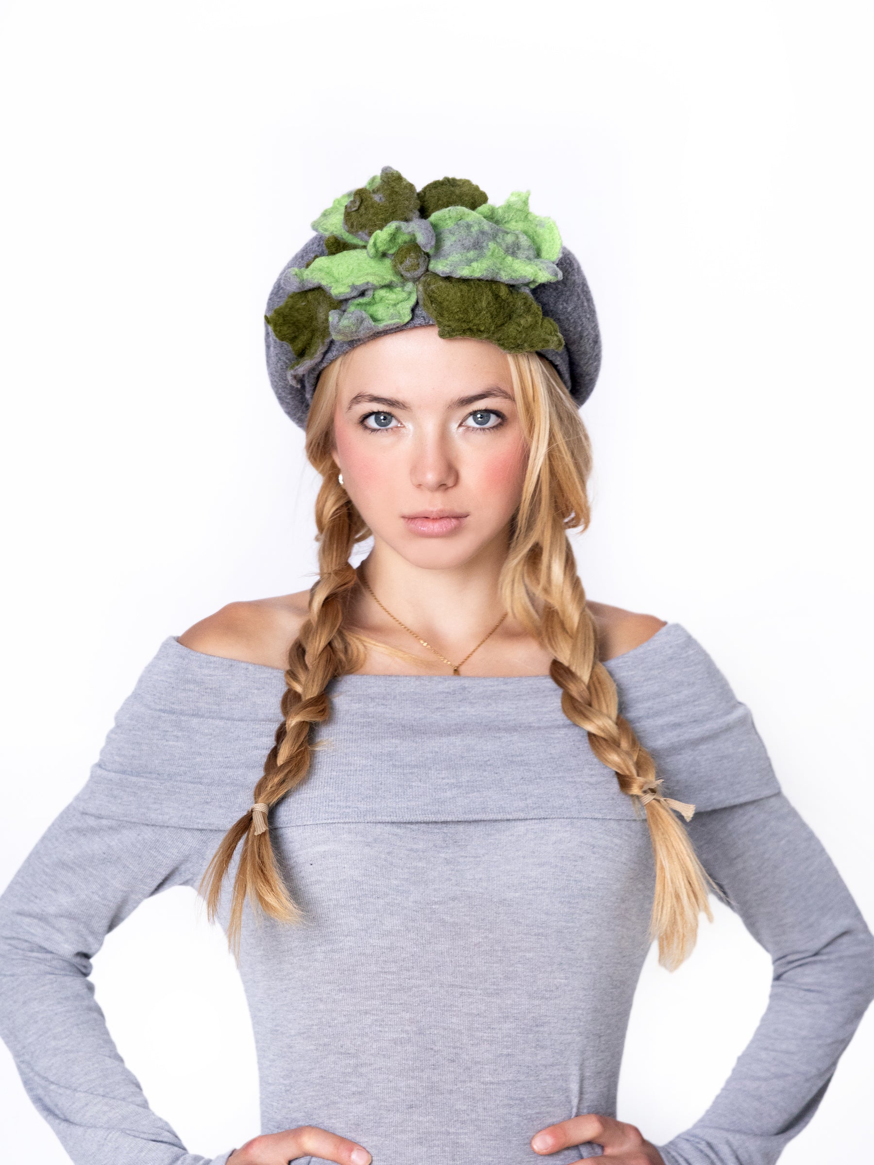 Model wearing a grey wool beret hat with handmade green felt floral detail, front view.