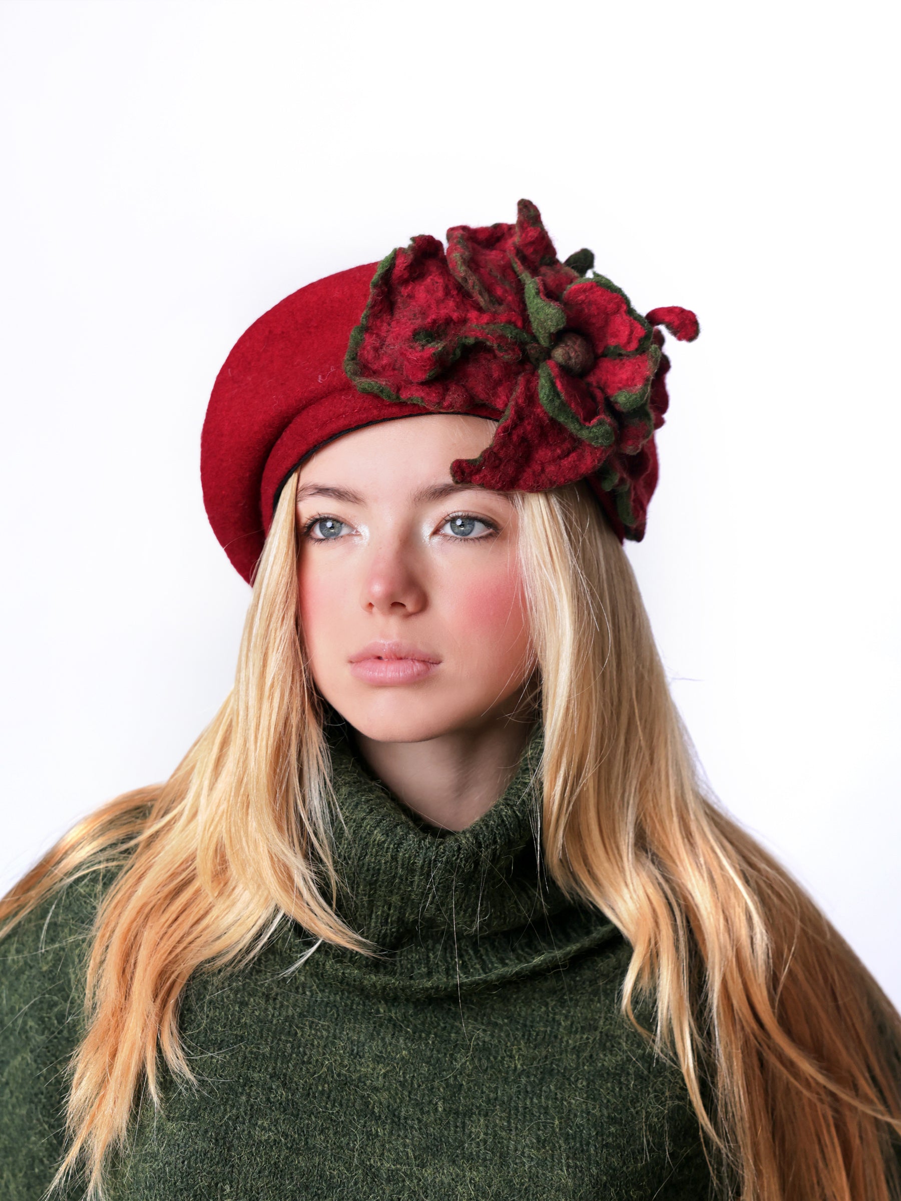 Model wearing a red wool beret hat with handmade red felt floral detail and green-edged leaves.