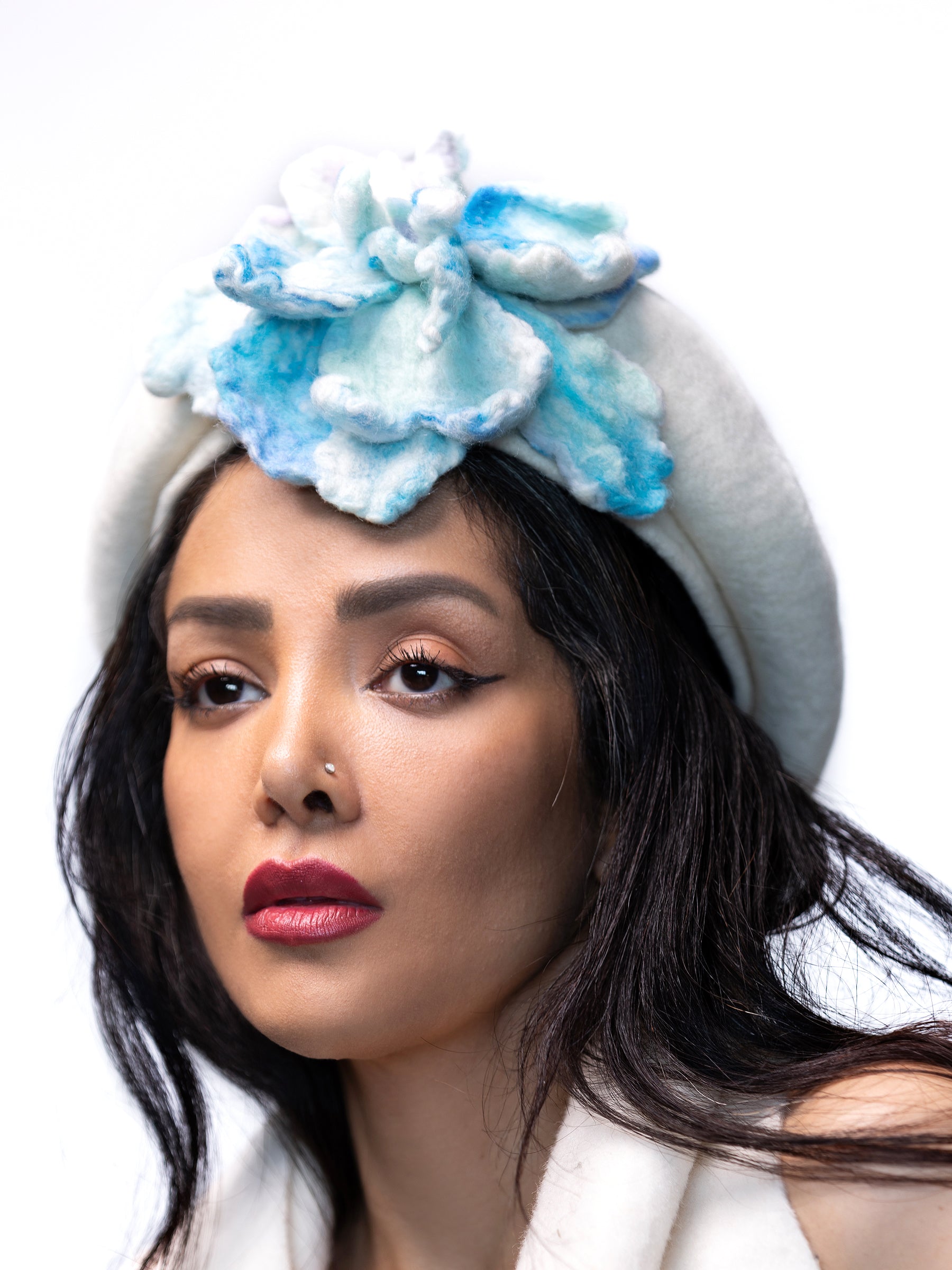 Side view of a white wool winter beret hat with handmade turquoise felt floral detail.
