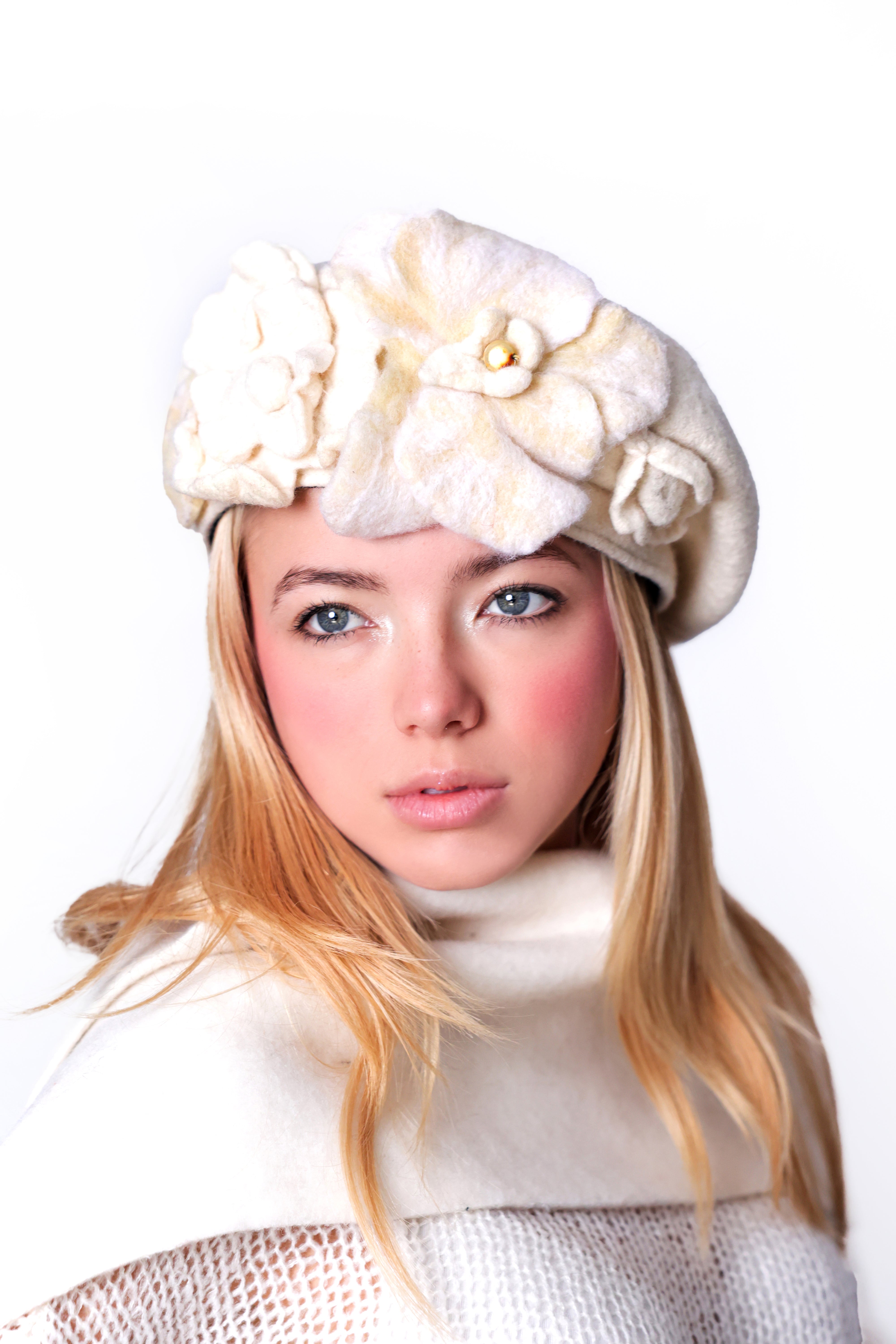 Model wearing a white wool beret hat with handmade ivory felt floral detail, front view.