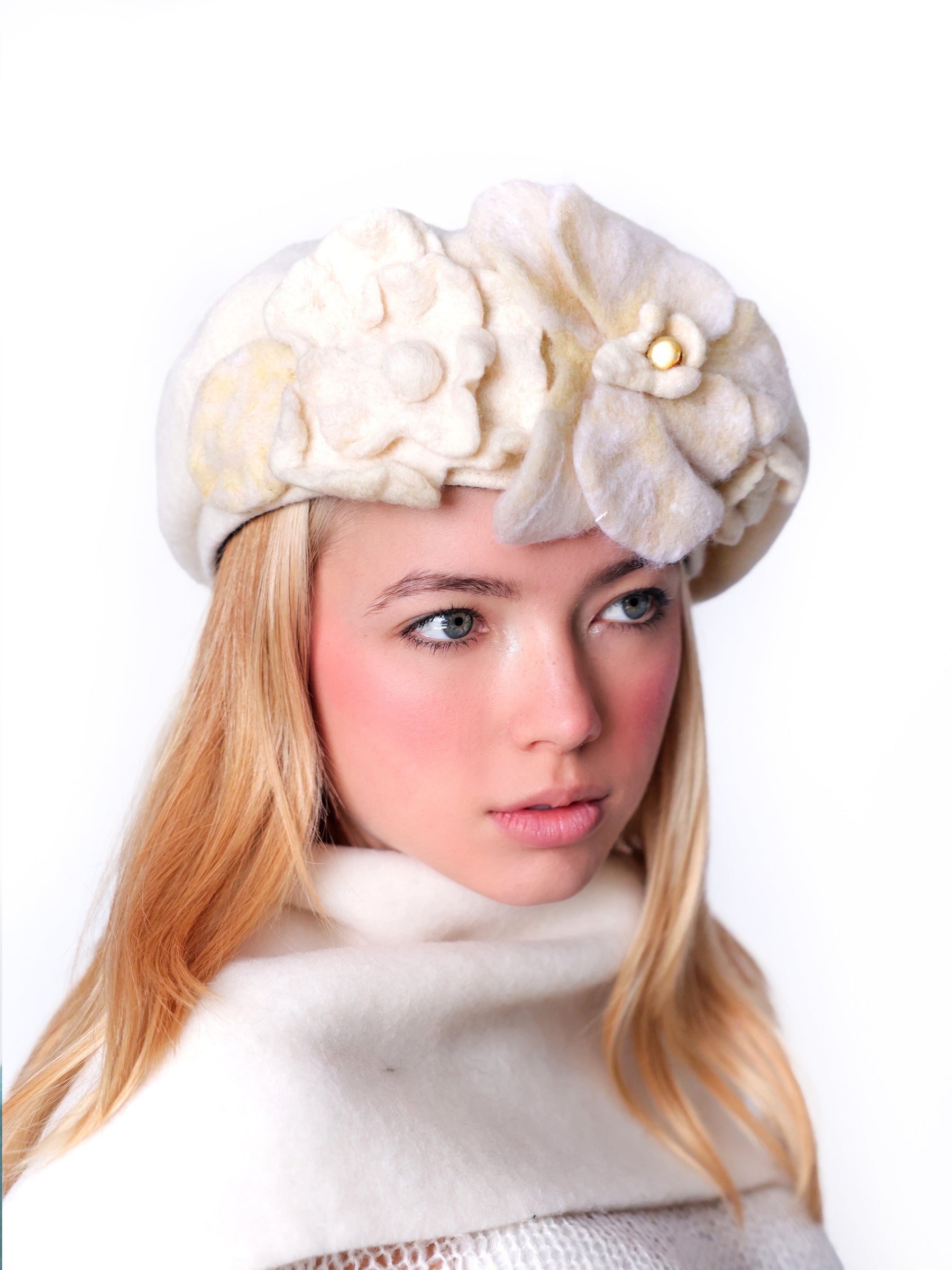 Side view of a white wool beret hat featuring sculptural handmade ivory felt flowers.