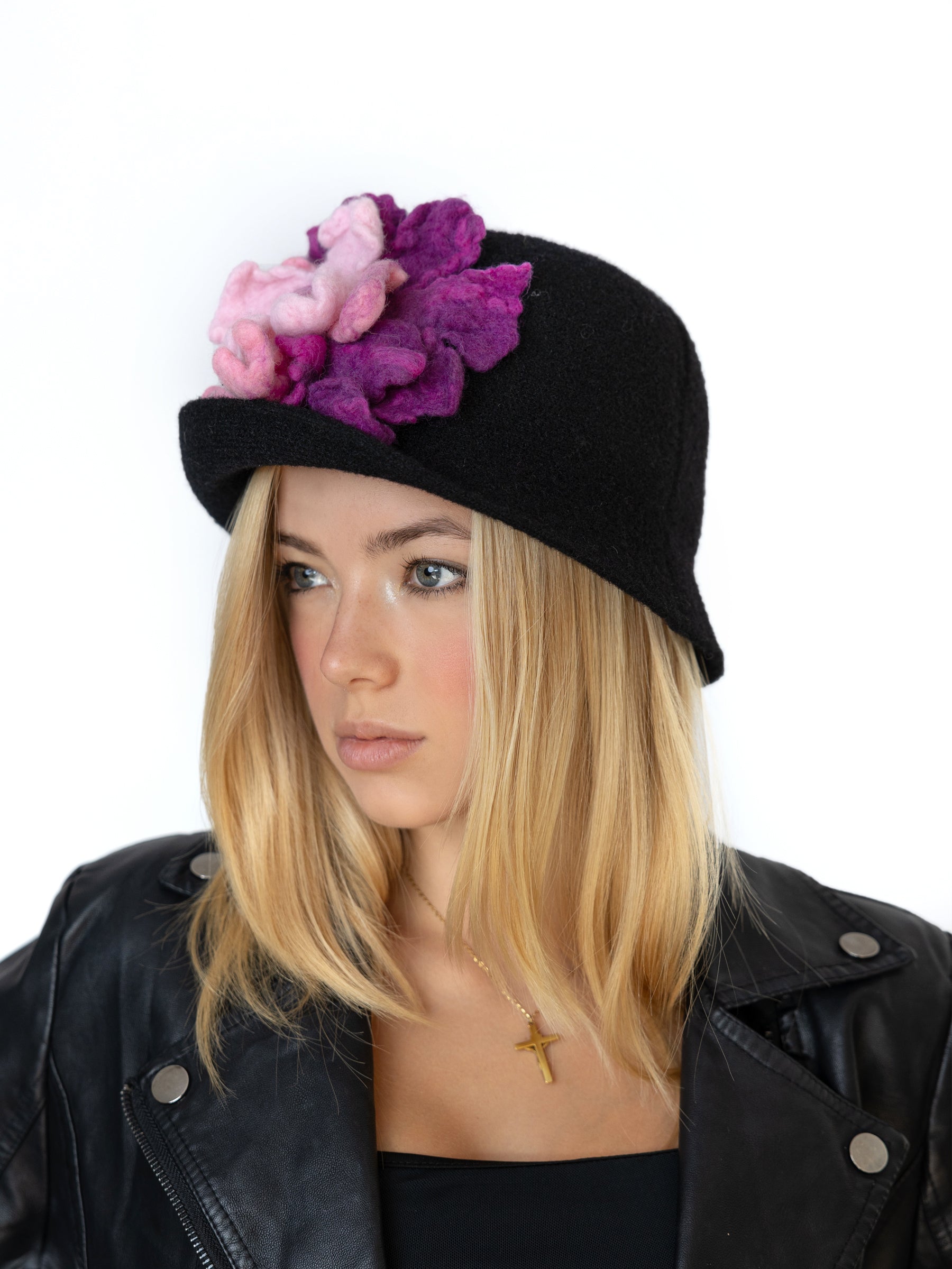 Side view of a black cloche hat featuring layered handmade felt flowers in pink and purple tones.