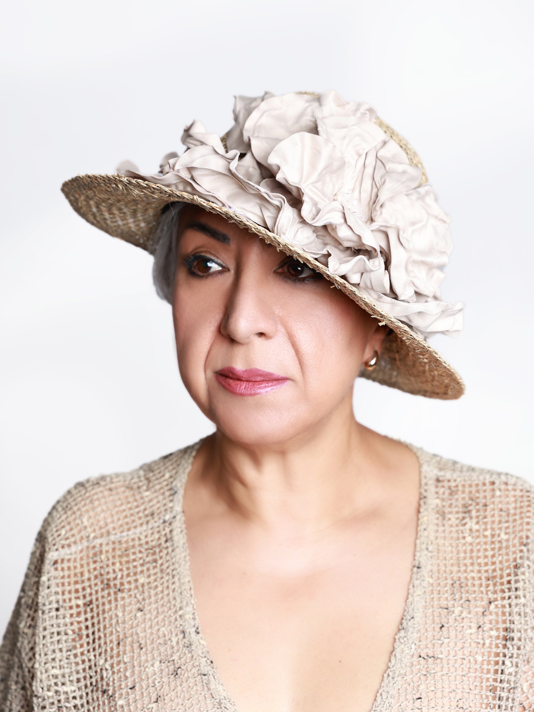 Angled side view of a natural straw sun hat featuring a handmade ivory satin flower, worn by a woman.