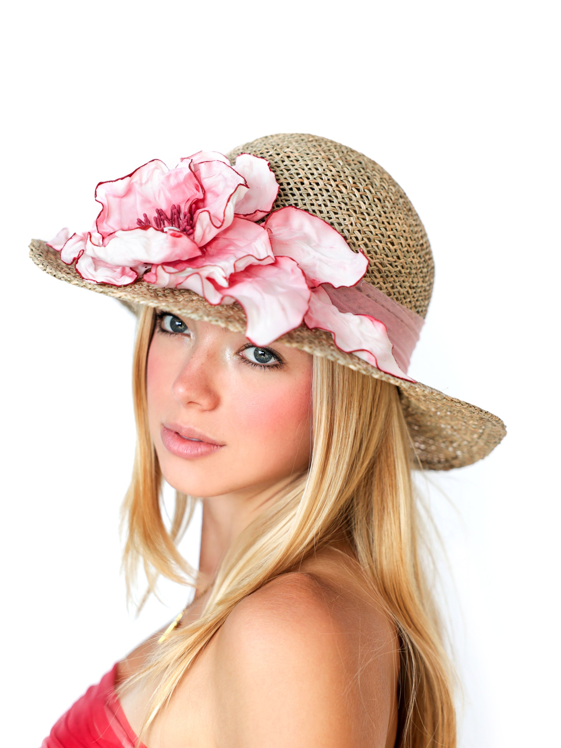 Angled view of a straw summer hat with handmade pink and white satin flower detail.