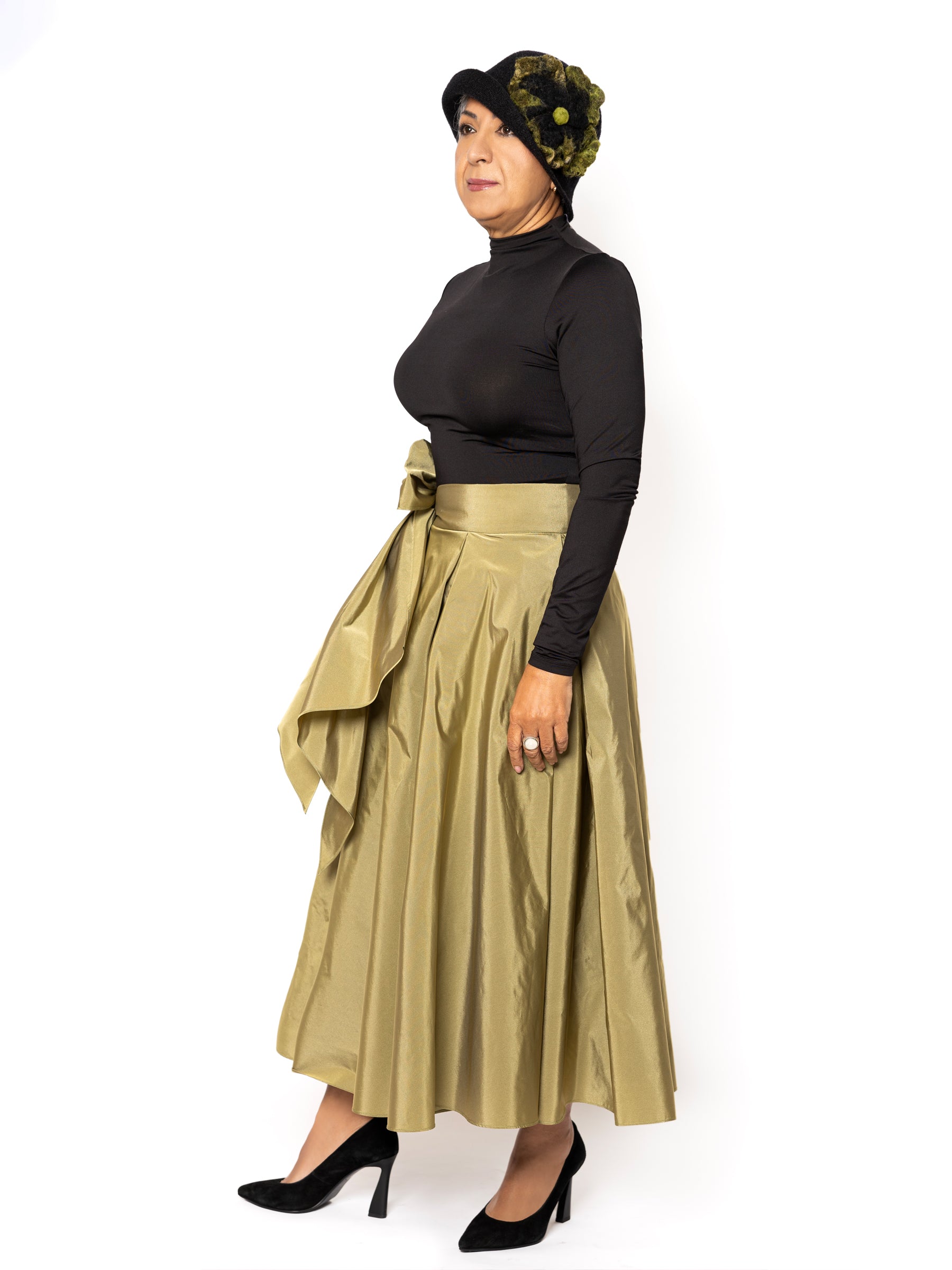 Female model wearing a fluid olive green midi skirt with soft sheen and structured drape by Romina Couture.